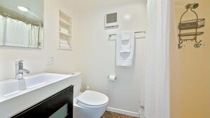 A bathroom with a white sink, toilet, and shower curtain. - Secluded Windansea Beach Rental Cottage (La Jolla)
