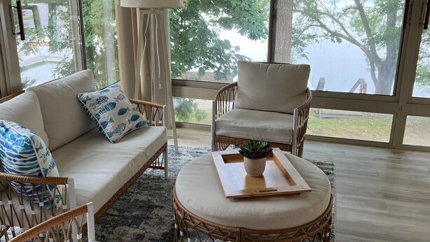 A spacious living room with a sofa, chairs, and a round table. Large windows offer a view of trees and a building outside. - Beautiful cottage on the lake
2 bedroom, 1 bath, sleeps 7-8 (Three Rivers)