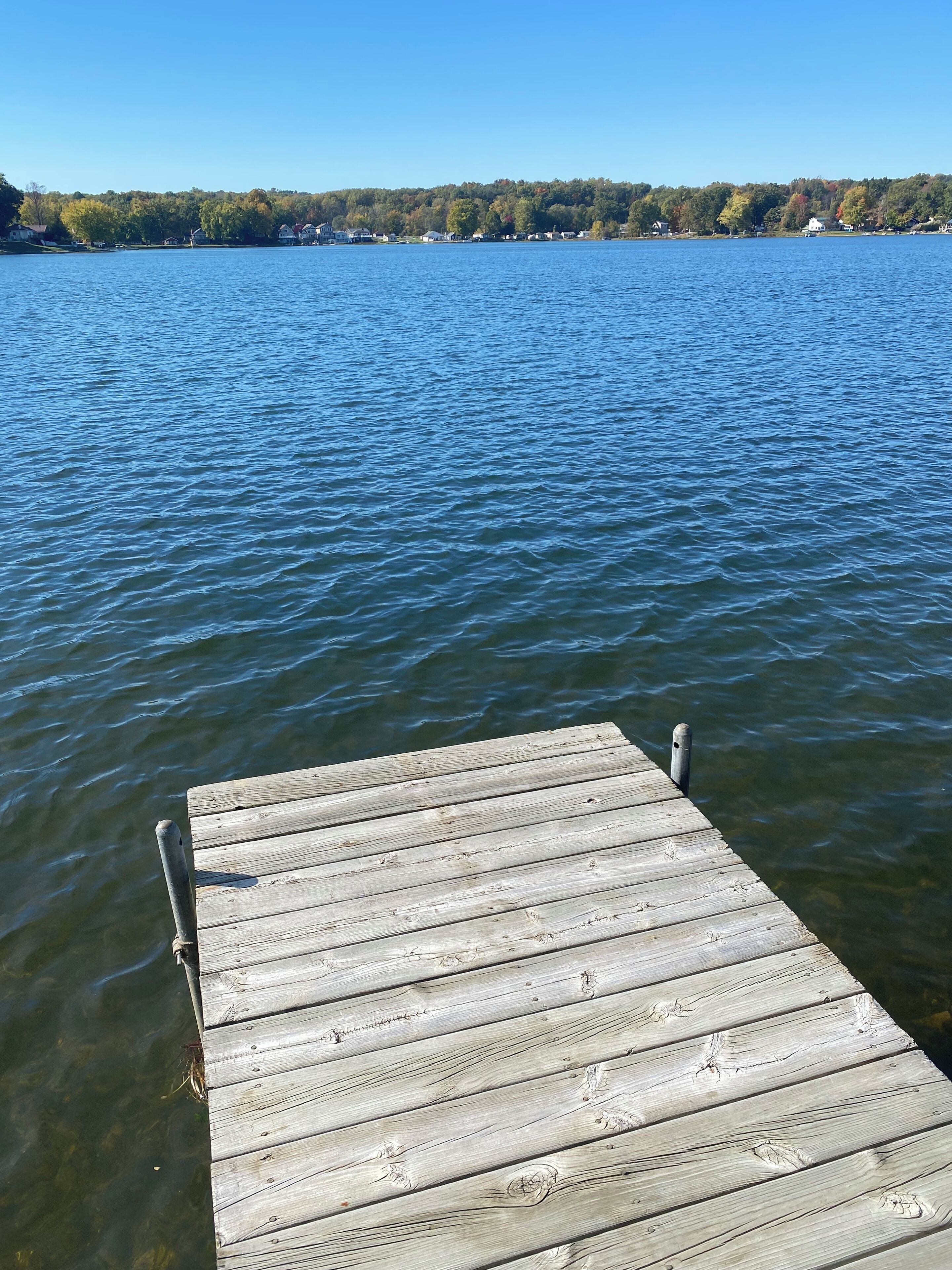 A wooden dock extending into a calm lake with a forested shoreline in the background.