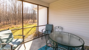 A room with a glass table and chairs, a view of a forest through large windows, and a white exterior wall.