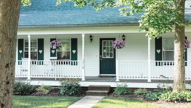 A white house with green shutters, a dark green front door, and a porch with white railings.