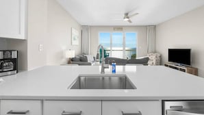 A modern kitchen with a central island, a built-in oven, and a large window offering a view of the ocean. - Seychelles 1302 | Beach Service Included | Parking Onsite | 2 Pools | Fitness Center (Panama City Beach)