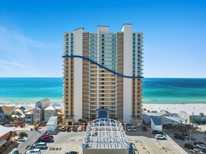 A high-rise hotel with a central atrium, a beach view, and a parking area in front. - Seychelles 1302 | Beach Service Included | Parking Onsite | 2 Pools | Fitness Center (Panama City Beach)