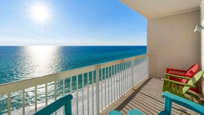 A balcony with a view of the ocean and beach, featuring a railing and colorful chairs. - Seychelles 1302 | Beach Service Included | Parking Onsite | 2 Pools | Fitness Center (Panama City Beach)