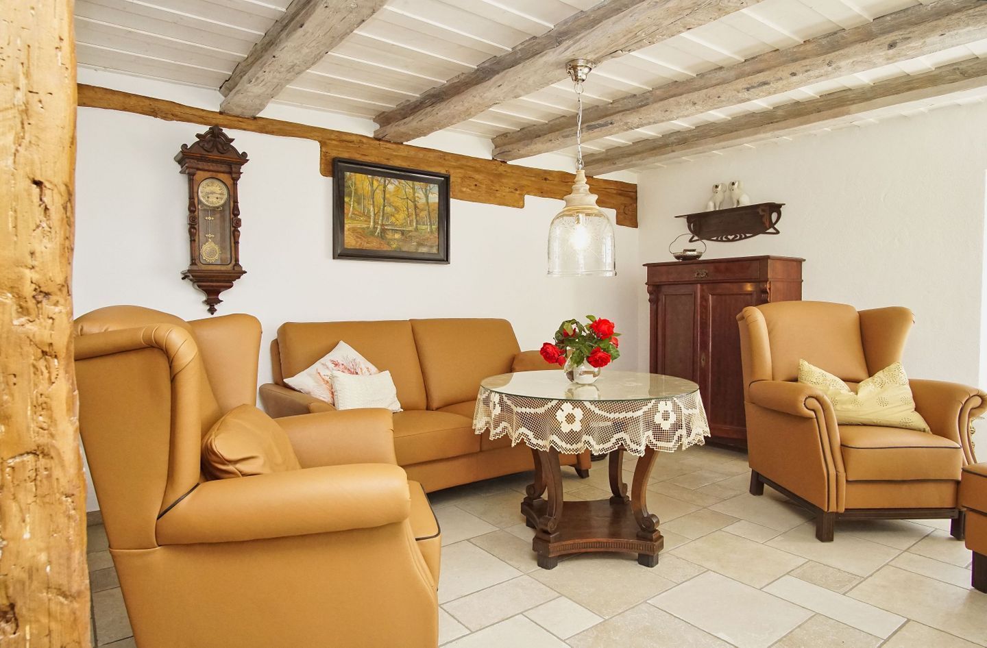 A living room with a sofa, armchair, and a table with a vase of flowers.
