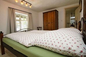 A bedroom with a bed, curtains, a wooden wardrobe, and a window. - Idyllic seaside location close to the beach, private bathing area - Gutshof Ostseeblick FeWo 04 - (Putbus)