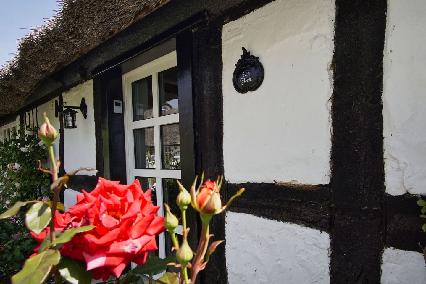 A traditional half-timbered building with a thatched roof, a white door, and a black sign with the text "Gute Gube".