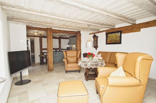 A living room with a TV, leather sofas, a coffee table, and a kitchen in the background.
