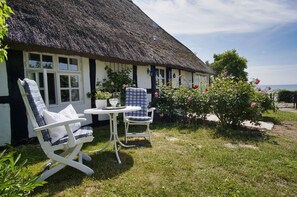 A thatched-roof house with two white chairs and a table outside. - Idyllic seaside location close to the beach, private bathing area - Gutshof Ostseeblick FeWo 04 - (Putbus)