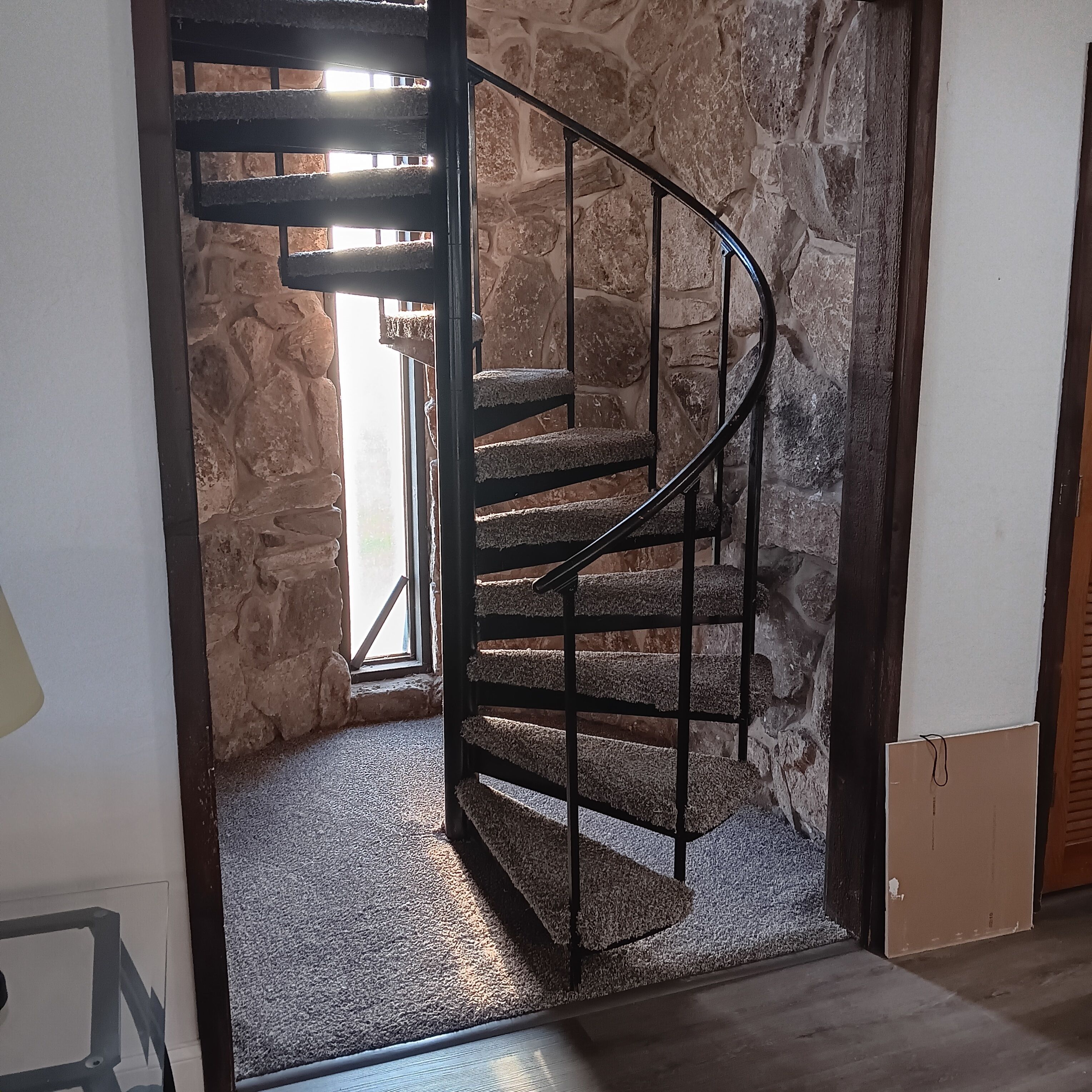 Un escalier en colimaçon, avec un mur en pierre en arrière-plan, mène à une pièce dotée d’une fenêtre.