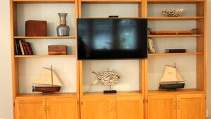 Een houten tv-meubel met een flatscreen-televisie, twee kleine zeilboten, een decoratieve vissenbeeldhouwing en enkele boeken.