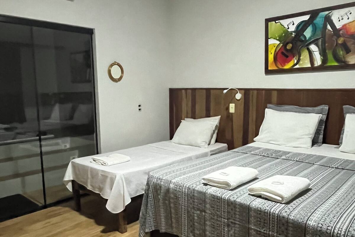 Ein Hotelzimmer mit zwei Einzelbetten, Holzboden, Klimaanlage, Wanduhr und einem farbenfrohen, abstrakten Gemälde.