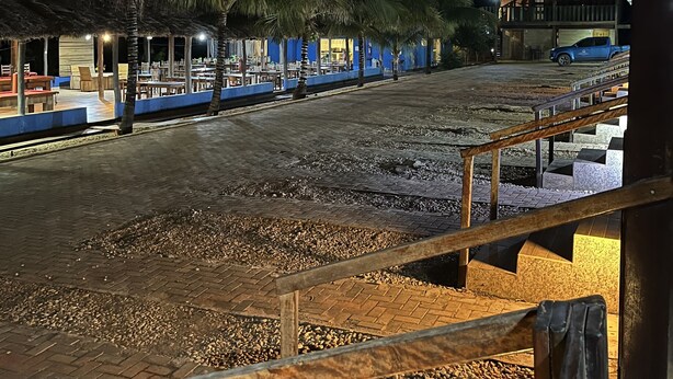 Vista nocturna de un resort con zonas de estar al aire libre, palmeras y un edificio de fachada azul.