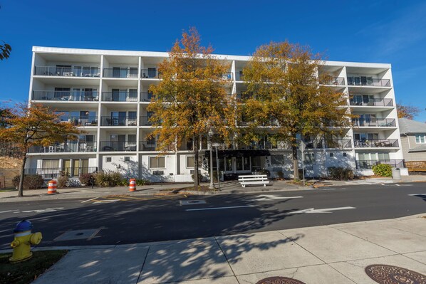 A multi-story residential building with balconies, a fire hydrant, and a bench on the sidewalk.