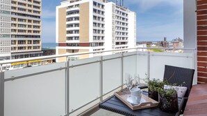 Ein Balkon mit Tisch, zwei Stühlen, einer Ablage mit Gläsern und einer Tasse sowie einem Blumentopf.