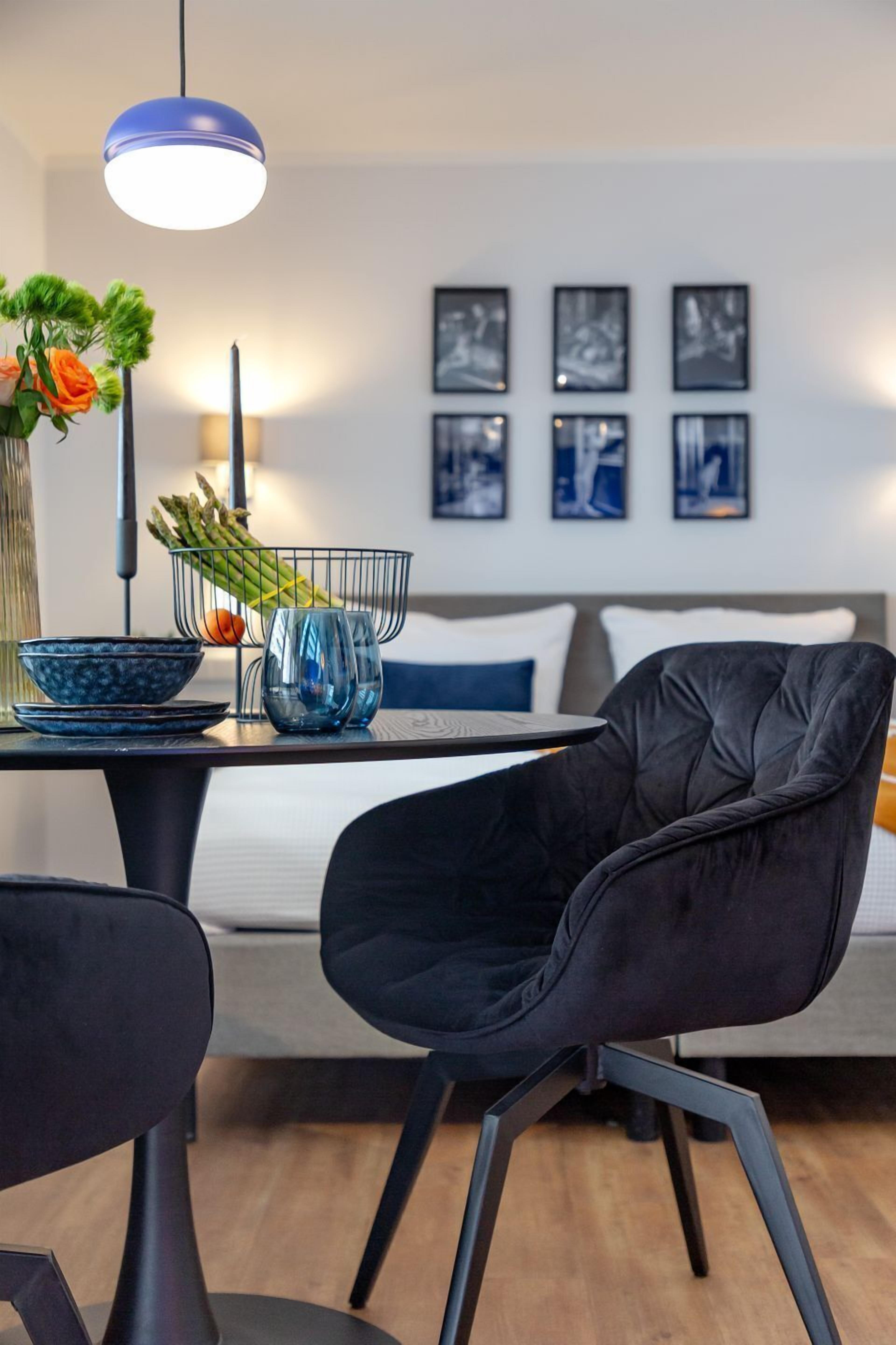A modern dining area with a table, chairs, a vase with flowers, and a basket of vegetables.