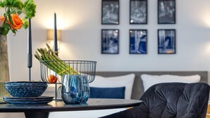 A modern dining area with a table, chairs, a vase with flowers, and a basket of vegetables. - Schickes Stranddomizil in der 3. Etage, in Direkter Lage zum Strand - Andreas-dirks-straße 5 (Sylt)