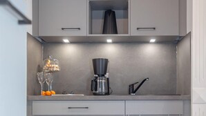 A compact kitchen with grey cabinets, a coffee maker, and a wine glass on the counter. - Schickes Stranddomizil in der 3. Etage, in Direkter Lage zum Strand - Andreas-dirks-straße 5 (Sylt)