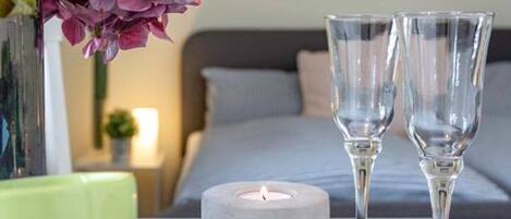 Une chambre avec un lit, une table de chevet sur laquelle se trouve une bougie, deux verres et une tasse verte.