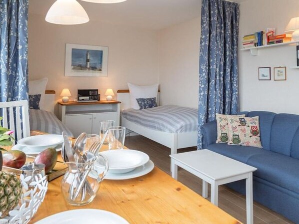 A compact hotel room with a bed, a small table with dining setup, a sofa, and a desk with a computer.