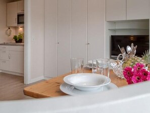 A modern kitchen with white cabinets, a wooden countertop, and a dining area set with plates, glasses, and cutlery.