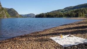 A lakeside view with a rocky shore, a blanket, and two bottles on the ground. - Bjørkstue by Interhome (Eikerapen)