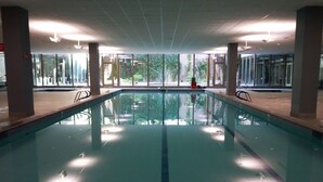 A large indoor swimming pool with clear glass walls, allowing views of the outdoors. - Optimal Camelback, Scottsdale Luxury Condo Living All Year Round! (Scottsdale)