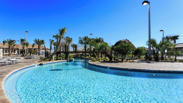 Une piscine d’un bleu éclatant, à bords incurvés, entourée de palmiers et de chaises longues.