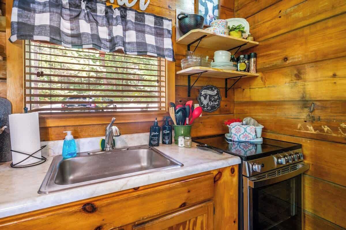 A kitchen with a stainless steel sink, wooden cabinets, a stove, and a window with blinds.