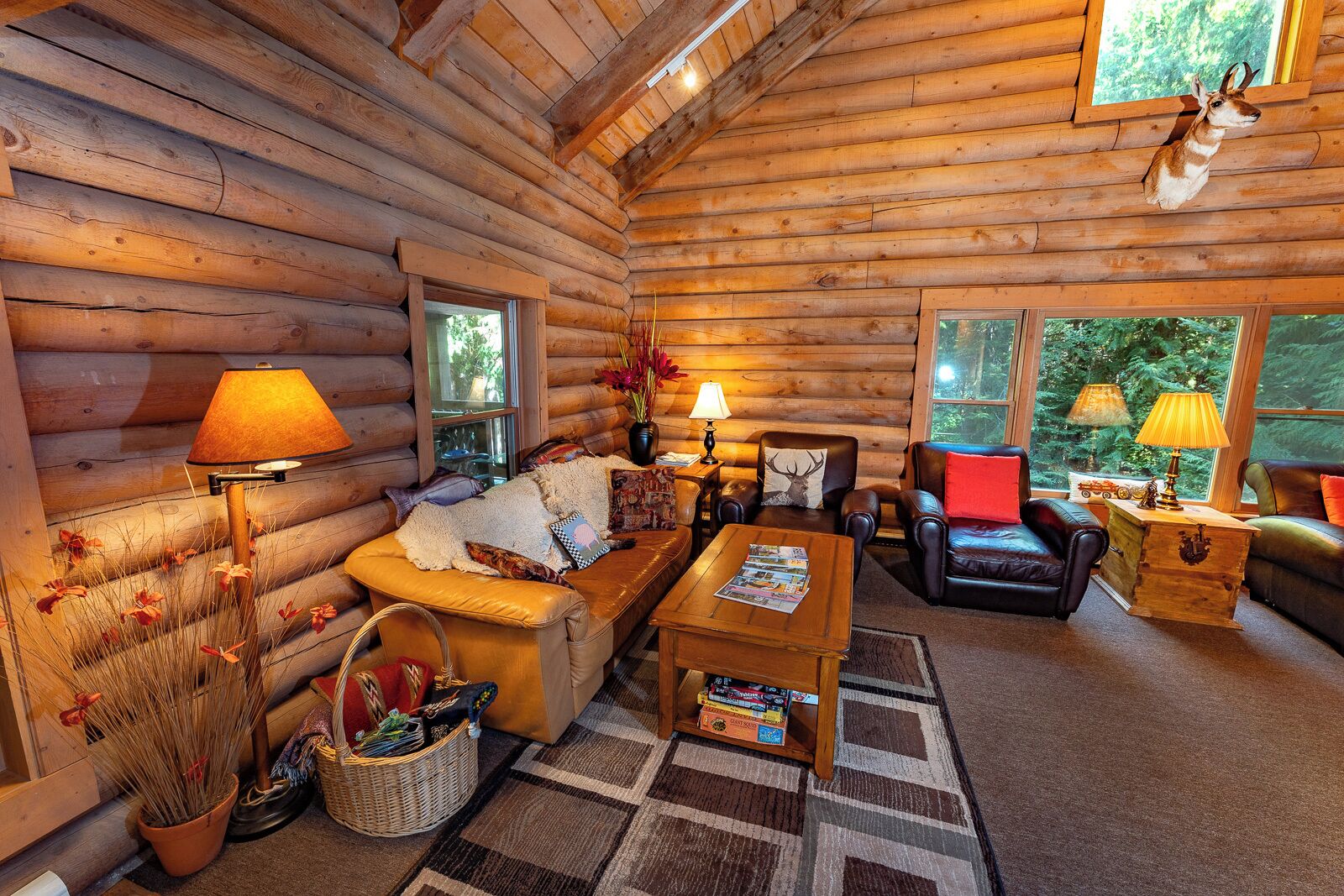 L’intérieur d’une cabane en rondins, avec un canapé, des fauteuils, une table basse et une cheminée.
