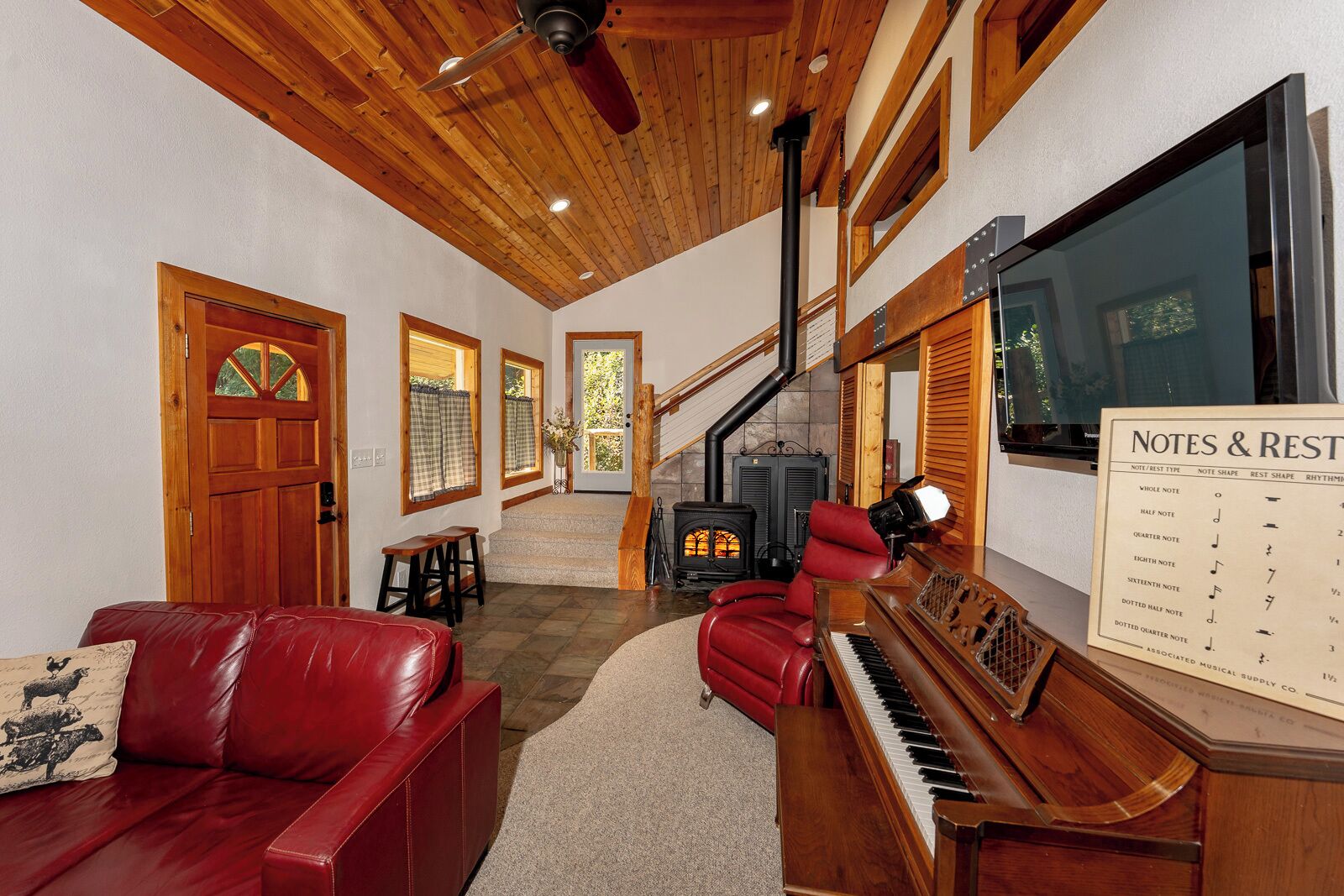 A spacious living room with a red leather sofa, a grand piano, a fireplace, and a large window.