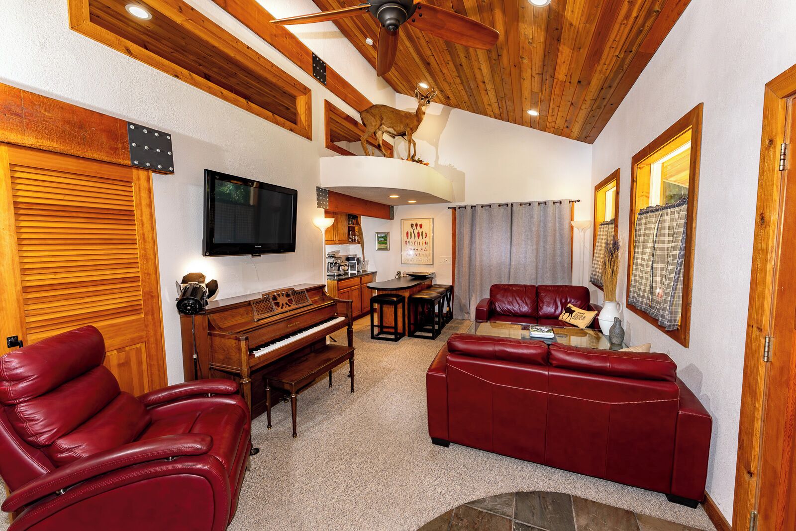 A living room with a wooden ceiling, a piano, red leather sofas, and a television.