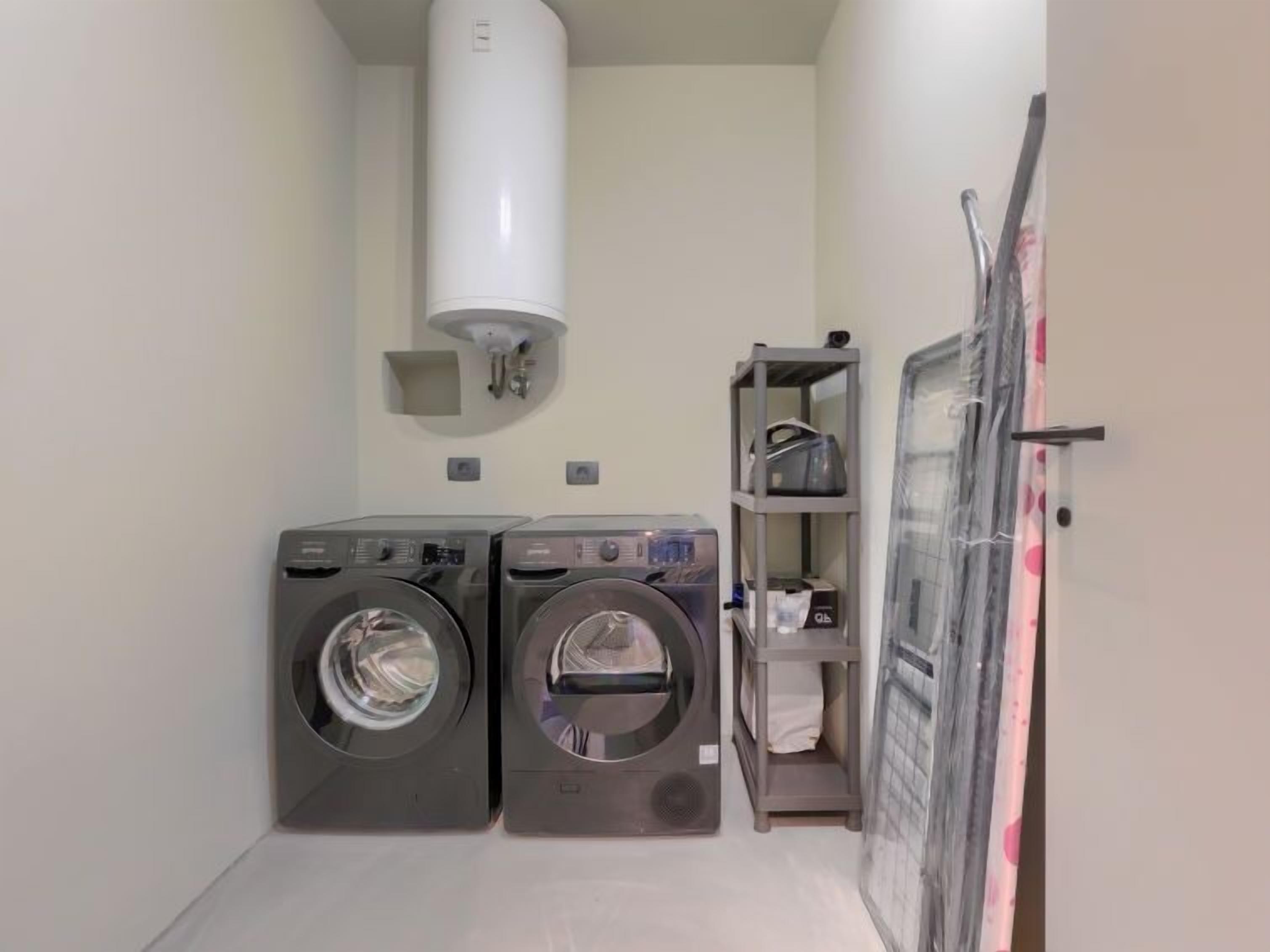 A laundry room with two front-loading washing machines, a water heater, and a shelf with towels.