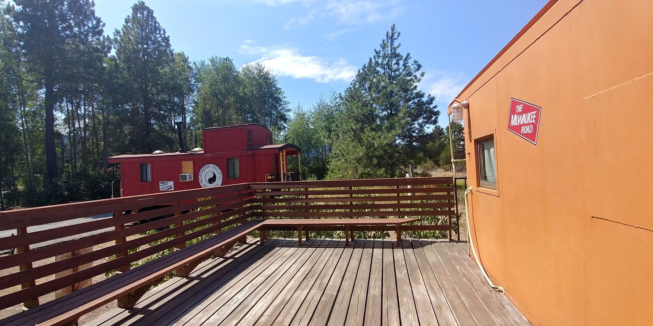 A wooden deck with benches, a red building labeled "Northern Pacific Radio," and a sign for "The Milwaukee Road."