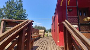 A wooden deck leading to a red building with a metal gate and a yellow handrail.
