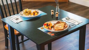 A dining table with two plates of food, a vase with flowers, and a magazine.
