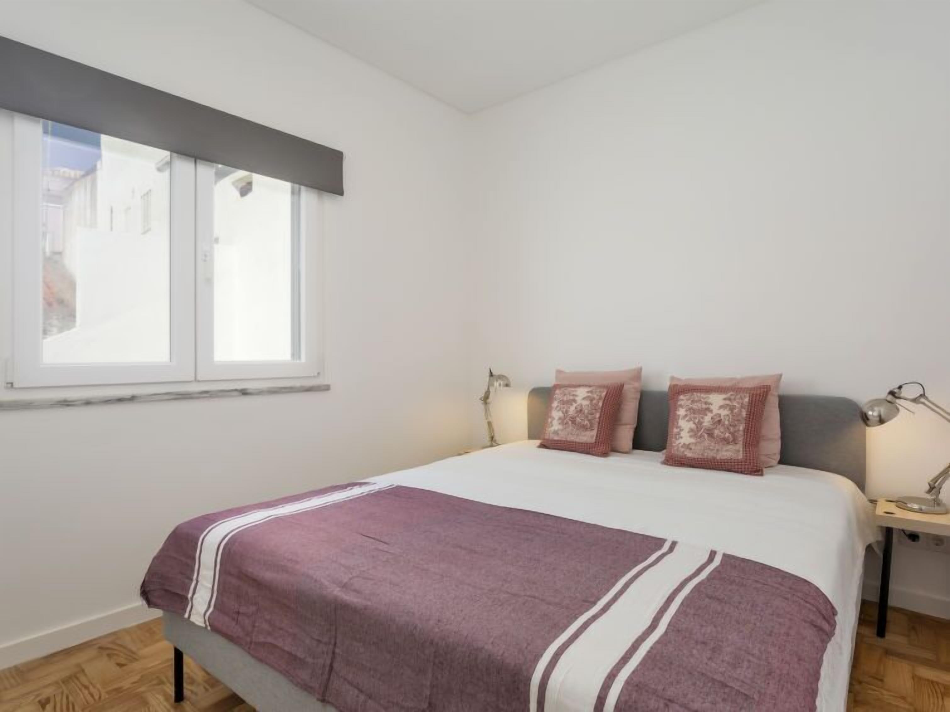 Un dormitorio con una cama, dos lámparas de noche, una ventana y vistas a edificios.