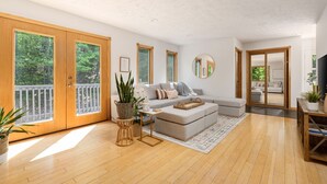 Un salon spacieux avec un canapé gris, un parquet en bois et de grandes fenêtres donnant sur un paysage verdoyant.