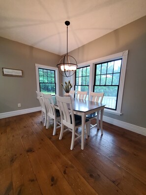 A dining area with a wooden table and white chairs, large windows with a view of greenery, and a pendant light fixture. - Private heated pool, ATV trails and shooting range on 20 acres (Mears)