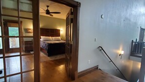 Ruime kamer met houten vloer, een bed met hoofdeinde, een plafondventilator en een trap met een leuning.