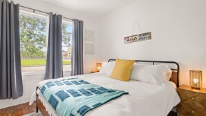 Ein Schlafzimmer mit einem Bett, einem Nachttisch, einem an der Wand befestigten Schild und einem Fenster mit Vorhängen.