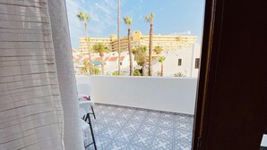 A balcony with patterned tiles, a white chair, and a view of buildings and palm trees. - Town house for 4/6 people (Torviscas Bajo)
