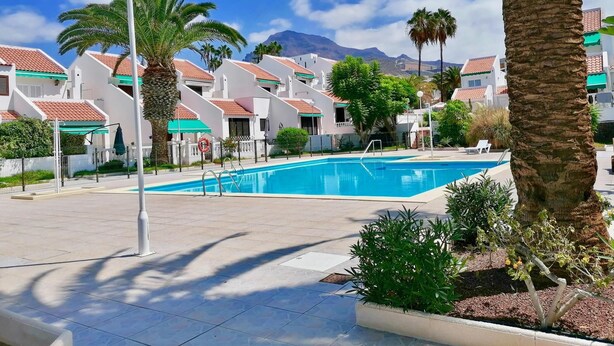 A swimming pool surrounded by palm trees and white buildings with red roofs. - Town house for 4/6 people (Torviscas Bajo)