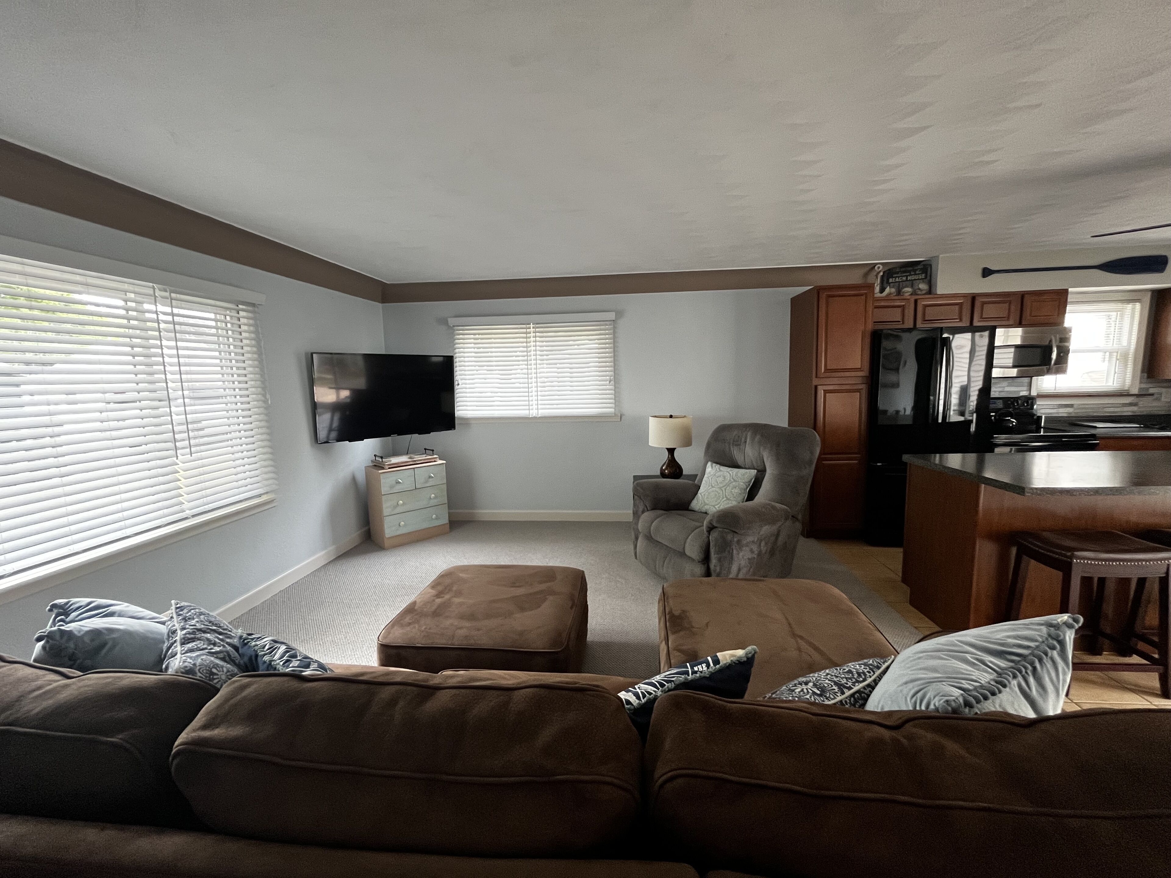 Una sala de estar con un sofá, un reposapiés y un televisor en la pared.