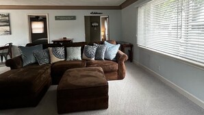 A spacious living room with a large sectional sofa, a small ottoman, and a dining area in the background. - Guest favorite Devils Lake Dock Private Fenced Yard Blackstone Grill (Manitou Beach-Devils Lake)