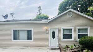 A single-story house with a beige exterior, a white front door, and two satellite dishes on the roof. - Guest favorite Devils Lake Dock Private Fenced Yard Blackstone Grill (Manitou Beach-Devils Lake)