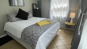 A neatly arranged bedroom with a bed, a ceiling fan, a bedside table with a lamp, and a window with curtains. - Guest favorite Devils Lake Dock Private Fenced Yard Blackstone Grill (Manitou Beach-Devils Lake)