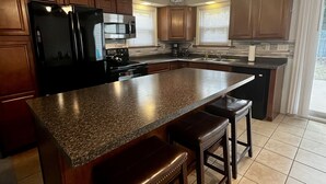 A modern kitchen with granite countertops, wooden bar stools, a built-in stove, and a ceiling fan. - Guest favorite Devils Lake Dock Private Fenced Yard Blackstone Grill (Manitou Beach-Devils Lake)