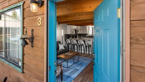 A wooden cabin with a blue door, a kitchen area with bar stools, and a living room with a sofa and coffee table. - Otters Den (West Yellowstone)
