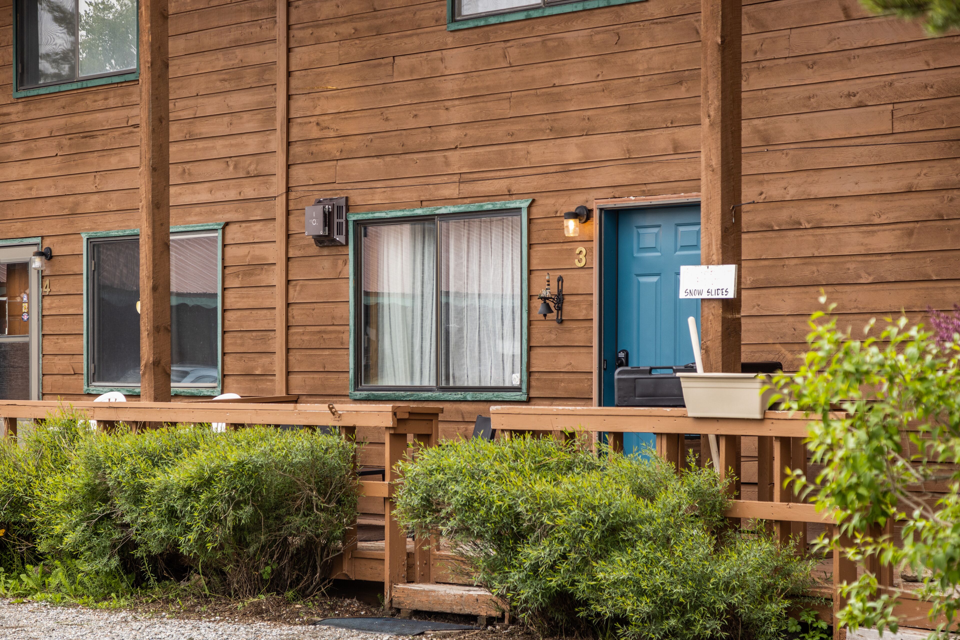 Een houten chalet met een blauwe deur, een bord waarop staat 'Snow Slides', en een klein terras met een bloempot.